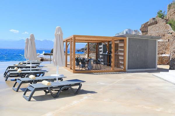 Akra Hotel Poolseite mit Lounge-Bereich, Liegestühlen und Sonnenschirmen am Meer.