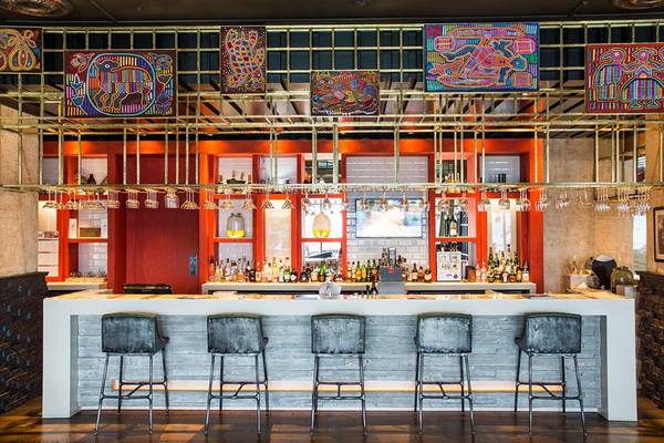 Innenansicht der Bar im Akra Hotel mit goldenen Metallrahmen, dekorativen Wandmalereien und grauen Barhockern.