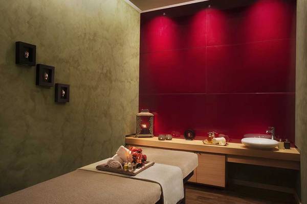 Spa-Behandlungsraum im Akra Hotel mit roten Wänden, zwei Massagetischen und einem Waschbecken.