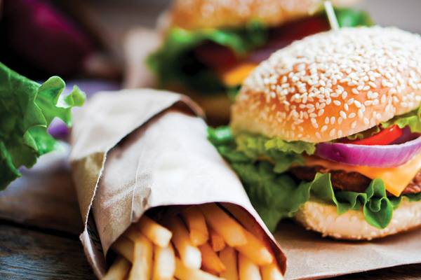 Zwei Burger und Pommes auf braunem Papier, eines mit Zwiebeln und Salat, das andere mit Tomaten und Salat.