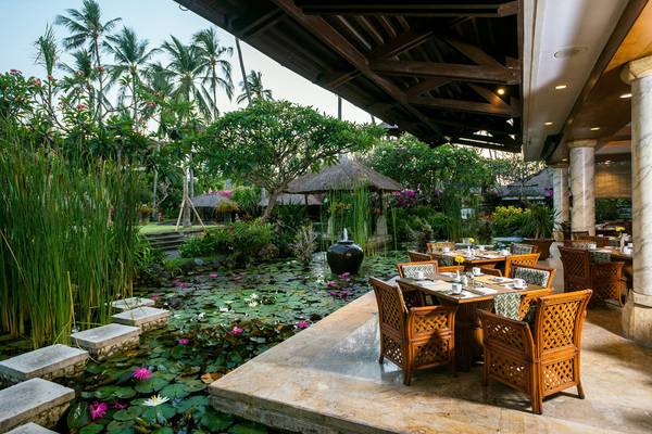 Außenterrasse des Nusa Dua Beach Hotel & Spa mit Tisch und Stühlen, umgeben von einem Teich mit Lotusblumen.