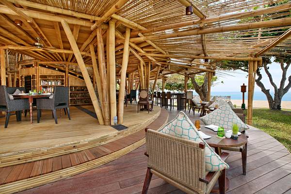 Foto der Bambus-Terrasse im Nusa Dua Beach Hotel & Spa mit Tischen, Stühlen und Blick auf den Strand.