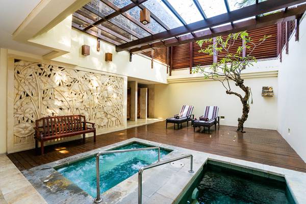 Innenpoolbereich des Nusa Dua Beach Hotel & Spa mit Holzboden, Lounge-Sesseln und Wasser.