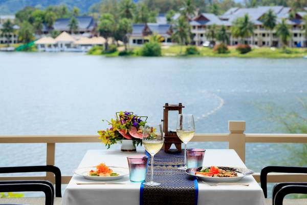 Terrasse im Dusit Thani Laguna Phuket mit einem Tisch, auf dem Essen, Wein und Dekor stehen.