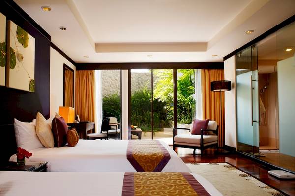Zwei Betten in einem Hotelzimmer des Dusit Thani Laguna Phuket, mit großen Fenstern und Ausblick auf den Garten.