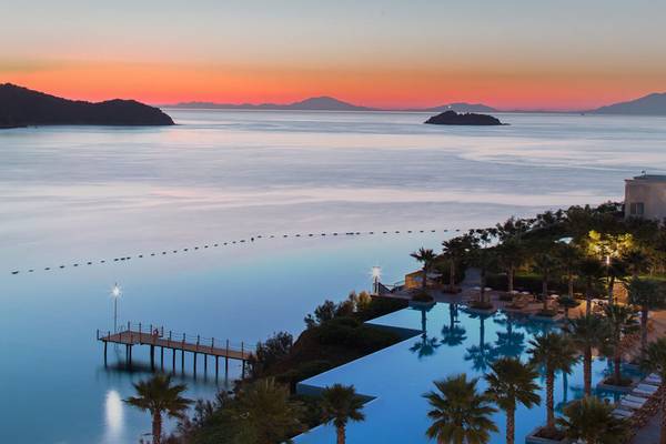 Aussicht auf das Xanadu Island Bodrum Hotel am Abend mit einem Swimmingpool, einer Sonnenuntergangslandschaft und einem Pier.