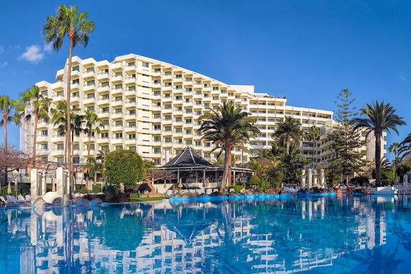 Das H10 Las Palmeras Hotel mit einem großen Swimmingpool und Sonnenliegen im Vordergrund.