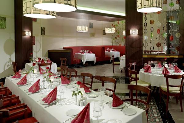 Innenansicht des Restaurants im Xanadu Island Bodrum Hotel mit geräumigen Tischen und Stühlen, roter Bestuhlung und dekorativen Kronleuchtern.