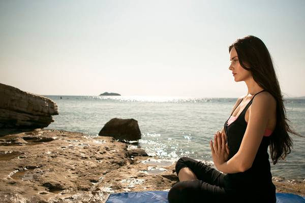 Frau in Yoga-Pose am Strand vor Meer-Hintergrund am frühen Morgen