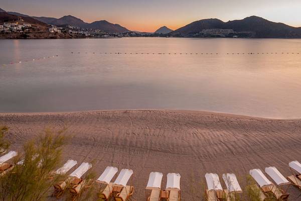Xanadu Island Bodrum Strand bei Sonnenuntergang mit Bergen im Hintergrund und weißen Sonnenliegen