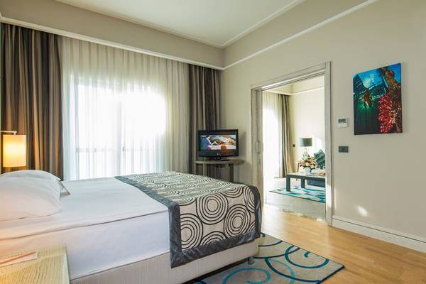 Schlafzimmer im Xanadu Island Bodrum Hotel mit Doppelbett, Fernseher und offener Tür zu einem Flur.