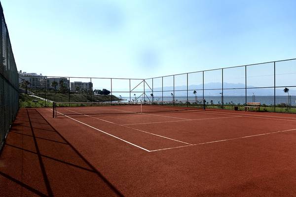 Tennisplatz im Xanadu Island Bodrum mit Blick auf das Meer und Gebäude im Hintergrund.