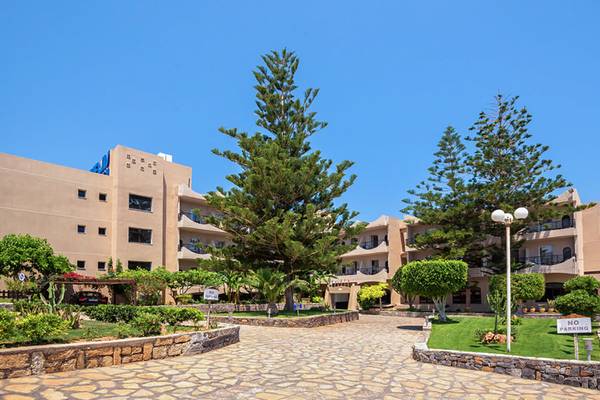Außenansicht des Themis Beach Hotels mit einem gepflasterten Eingangsbereich, hohen Bäumen und gepflegten Gärten.