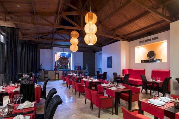 Innenbereich des BlueBay Villas Doradas Restaurants mit roten Stühlen, Tischen und dekorativen Lampen.