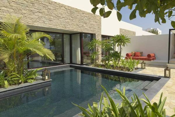 Außenbereich des Al Baleed Resort Salalah by Anantara mit Swimmingpool, Pflanzen und Möbeln.