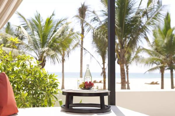 Aussicht auf den Strand vom Al Baleed Resort Salalah by Anantara mit einem Tisch, Früchten und einem roten Kissen.