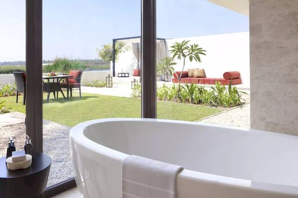 Innenansicht eines Badezimmers im Al Baleed Resort Salalah by Anantara mit Badewanne und Glastüren zum Garten