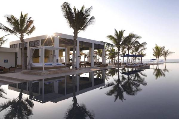Außenbereich des Al Baleed Resort Salalah mit Infinity-Pool und Sonnenliegen