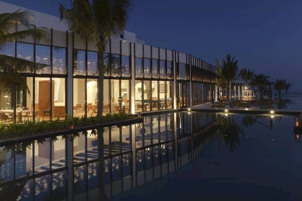 Nachtansicht des Al Baleed Resort Salalah by Anantara mit illuminiertem Gebäude und Pool.