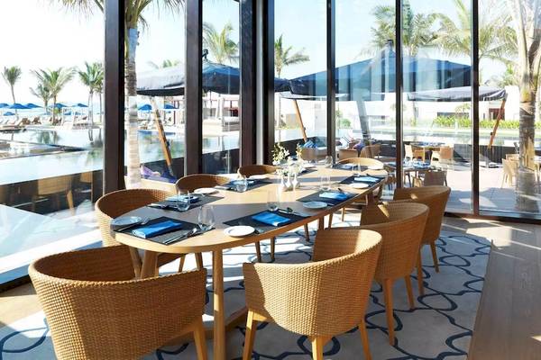 Innenansicht des Restaurants im Al Baleed Resort Salalah by Anantara mit großen Fenstern und Blick auf den Pool.