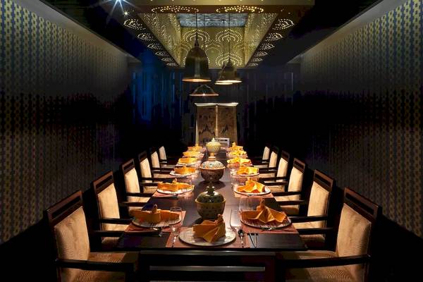 Speisesaal im Al Baleed Resort Salalah by Anantara mit langen Tisch, gedeckten Tellern und dekorativen Wandmustern.