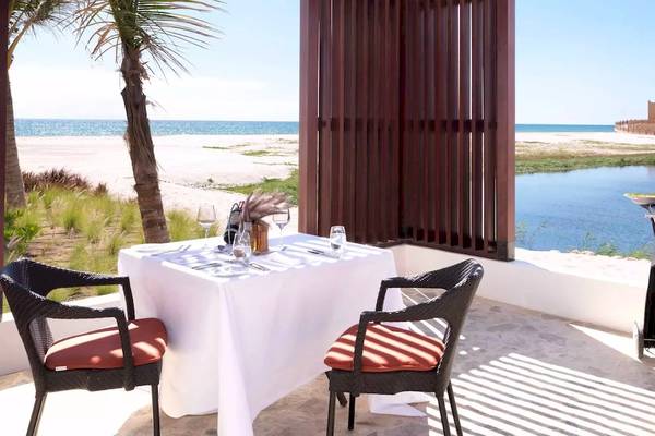 Außenbereich des Al Baleed Resort Salalah mit Tisch, Grill und Blick auf den Strand und das Meer.