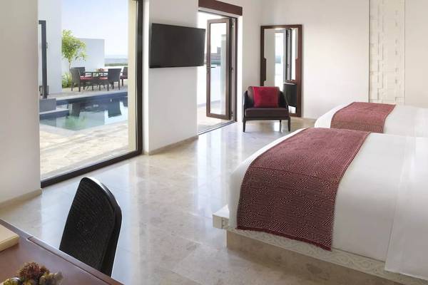 Schlafzimmer im Al Baleed Resort Salalah by Anantara mit zwei Betten, einem Tisch, einem Fernseher und einem Pool draußen.