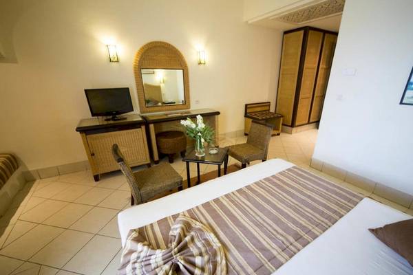 Hotelzimmer im Green Palm mit Bett, Fernseher, Tisch und Dekoblumen.