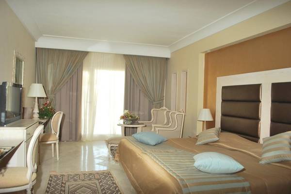 Luxuriöses Hotelzimmer mit Doppelbett, Fernseher, Tisch mit Blumen und Stühle im Green Palm Hotel.