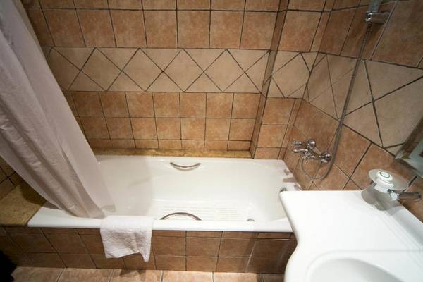 Ein Badezimmer mit einer Badewanne, einer weißen Dusche, braunen Fliesen und einem Spiegel.