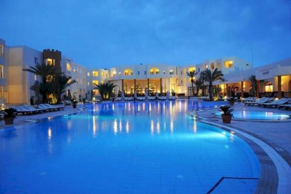 Der Poolbereich des Green Palm Hotels bei Nacht mit illuminiertem Gebäude und Loungeliegen.