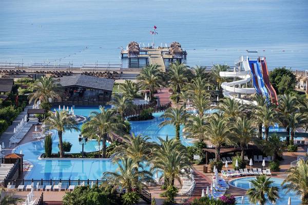 Luftaufnahme des Poolbereichs des Liberty Hotels Lara mit mehreren Schwimmbecken, Wasserrutschen und Sonnenliegen am Meer.