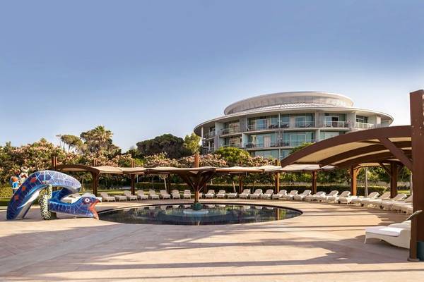 Außenbereich des Calista Luxury Resort mit Pool, Liegestühlen und dekorativer Skulptur.