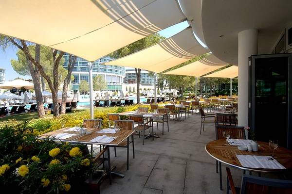 Außenbereich des Calista Luxury Resorts mit überdachten Tischen und Stühlen, umgeben von Bäumen und Blumen.
