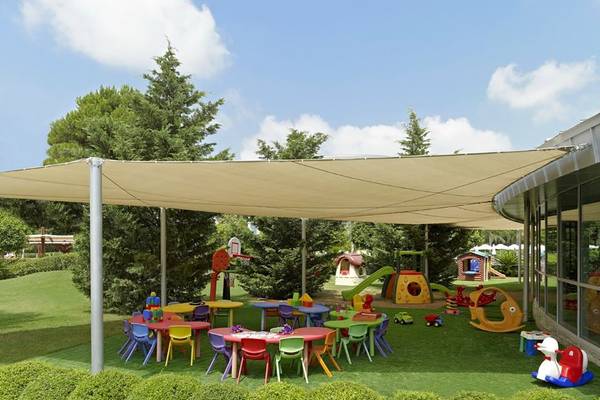 Spielplatz im Freien des Calista Luxury Resort mit bunten Tischen und Stühlen unter einem Sonnensegel.