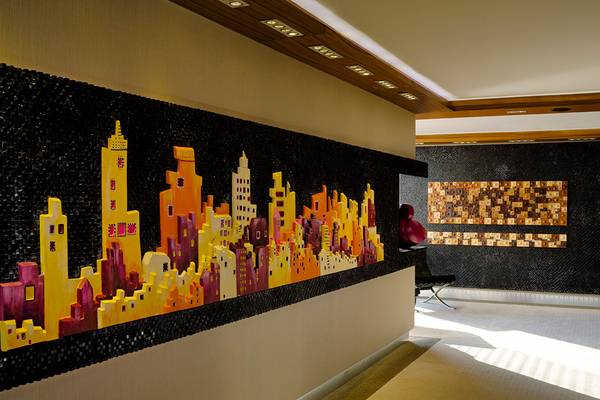 Eine Stadtlandschaft aus bunten Mosaiksteinen auf der Wand in einem Hotelflur.