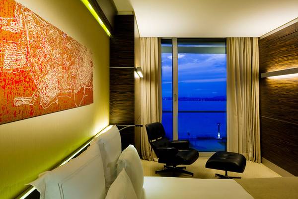 Hotelzimmer mit moderner Einrichtung, großem Bett, Sitzecke und Aussicht auf Wasser.