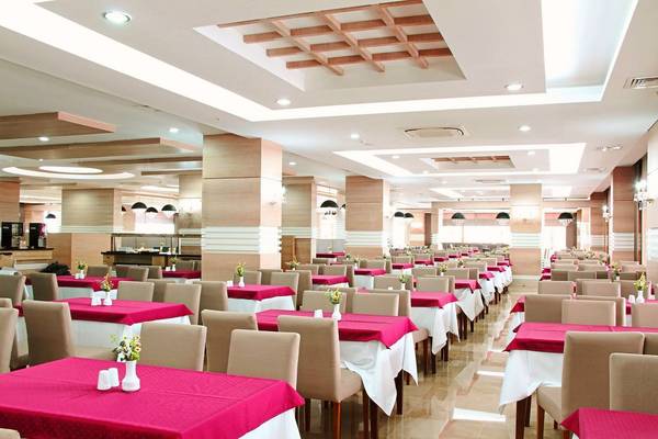 Innenbereich eines Restaurants im Hotel Adalya Ocean Deluxe mit vielen Tischen und Stühlen, dekoriert mit roten Tischdecken und Blumen.