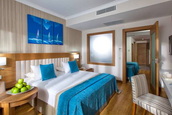 Innenansicht eines Doppelzimmers im Adalya Ocean Deluxe Hotel mit großem Bett, Nachttischen und Kunstwerken an der Wand.