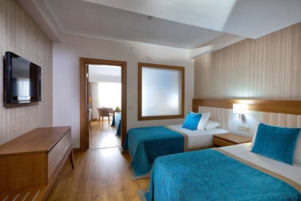 Innenansicht eines Doppelzimmers im Adalya Ocean Deluxe Hotel mit zwei Betten, Nachttischen, Fernseher und Spiegeltür.