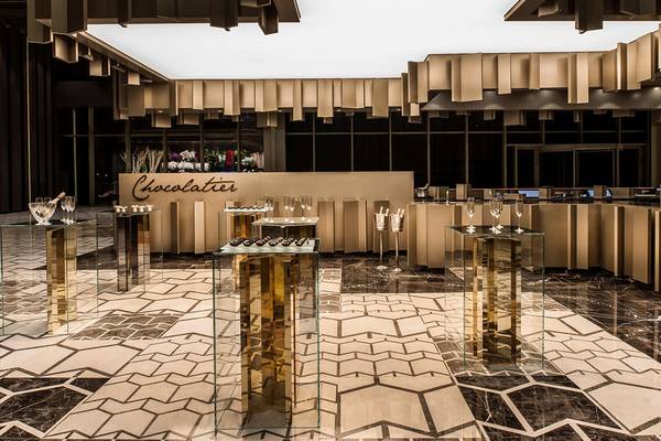Ein eleganter Bereich im Maxx Royal Kemer Resort mit Glastischen, goldenen Säulen und einer Theke mit dem Wort Chocolatier.