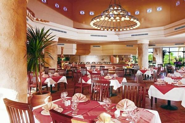 Innenansicht des Restaurants im Charmillion Garden Aqua Park mit runden Tischen und Stühlen, Pflanzen und Deckenleuchte.