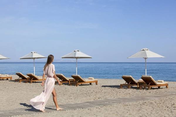 Frau am Strand des Aquila Rithymna Beach Hotels, umgeben von Sonnenliegen und Sonnenschirmen