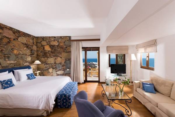 Schlafzimmer im Aquila Rithymna Beach Hotel mit Meerblick und Steinmauer.