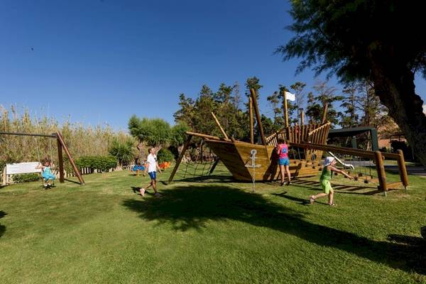 Kinder spielen auf einem Spielplatz im Freien, der ein Piratenschiff und eine Schaukel hat.