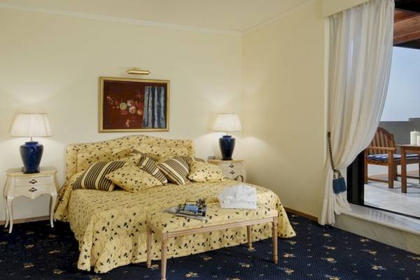 Schlafzimmer im Aquila Rithymna Beach Hotel mit gelber Bettwäsche, Nachttischen und Lampen.