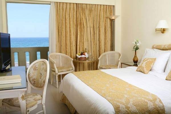 Hotelzimmer im Aquila Rithymna Beach mit Balkon und Meerblick, inklusive Bett, Sesseln, Tisch und Fernseher.