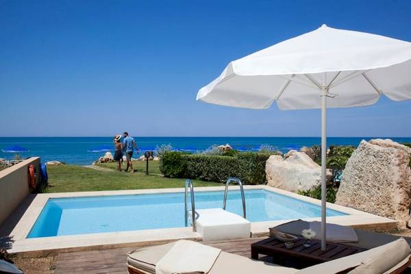 Ein Swimmingpool mit einem Paar, das auf der linken Seite steht, während ein großer weißer Sonnenschirm auf der rechten Seite steht.