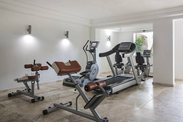 Fitnessraum im Falkensteiner Resort Capo Boi mit Geräten und Blick auf Außenbereich