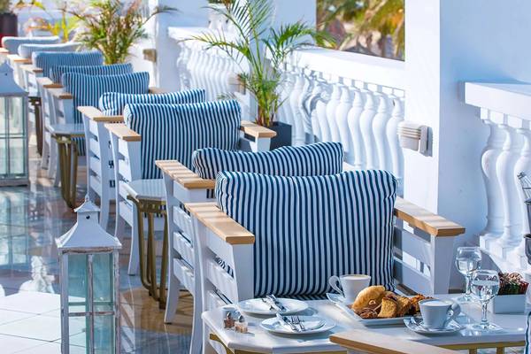 Terrasse des Minos Imperial Beach Resorts mit blau-weiß gestreiften Stühlen und Tischen, gefüllt mit Frühstücksplatten und Getränken.